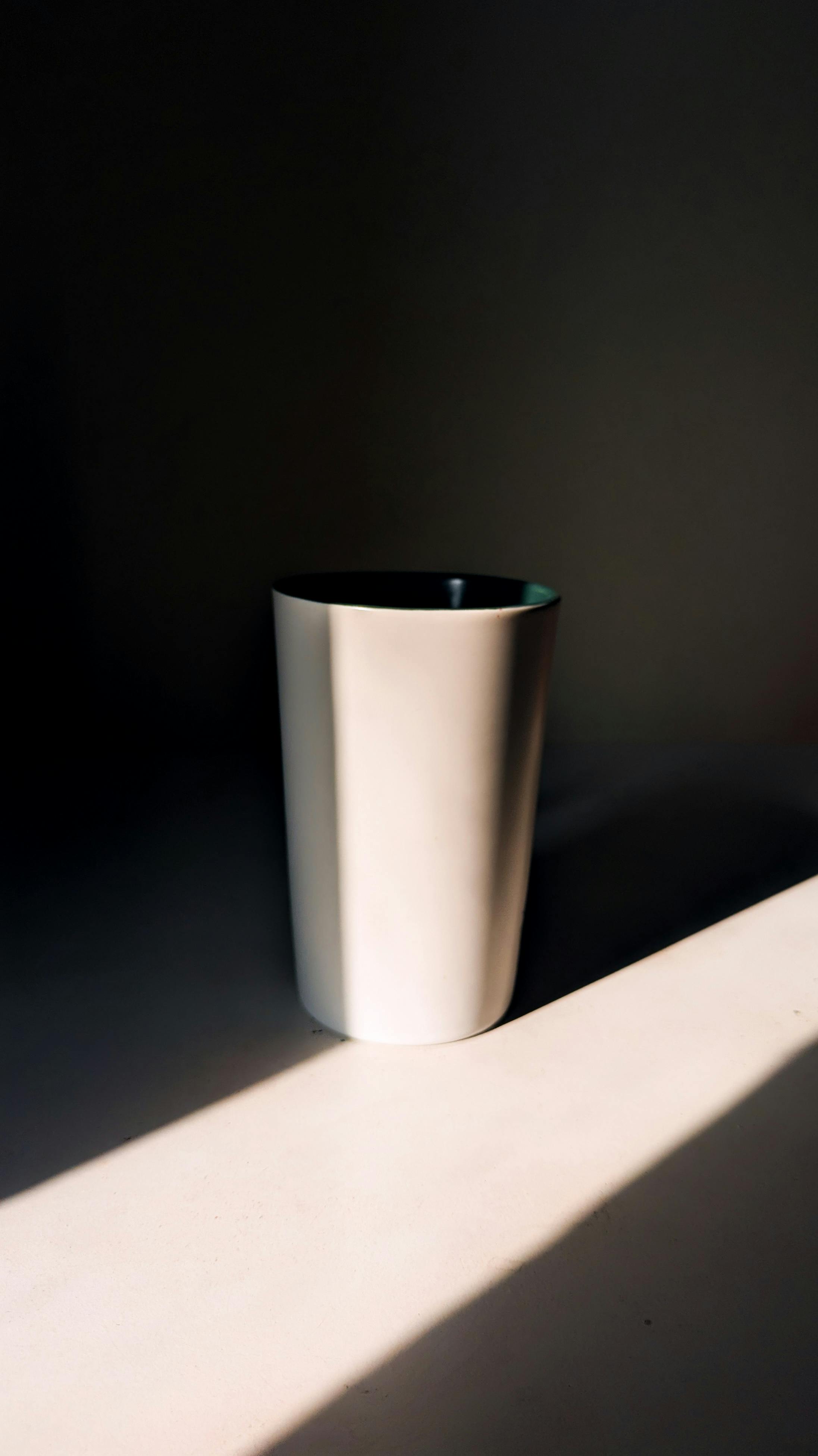 A pale ceramic cup on a paper background, with a long hard shadow cast by a single directional light.